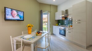 A modern kitchen with white cabinets, a built-in oven, and a dining area with a table set for two. - Casa Smeralda a 200 mt Dal Mare (Augusta)