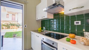 A kitchen with a green tiled backsplash, a stainless steel range hood, a built-in oven, and a window overlooking a garden. - Casa Smeralda a 200 mt Dal Mare (Augusta)