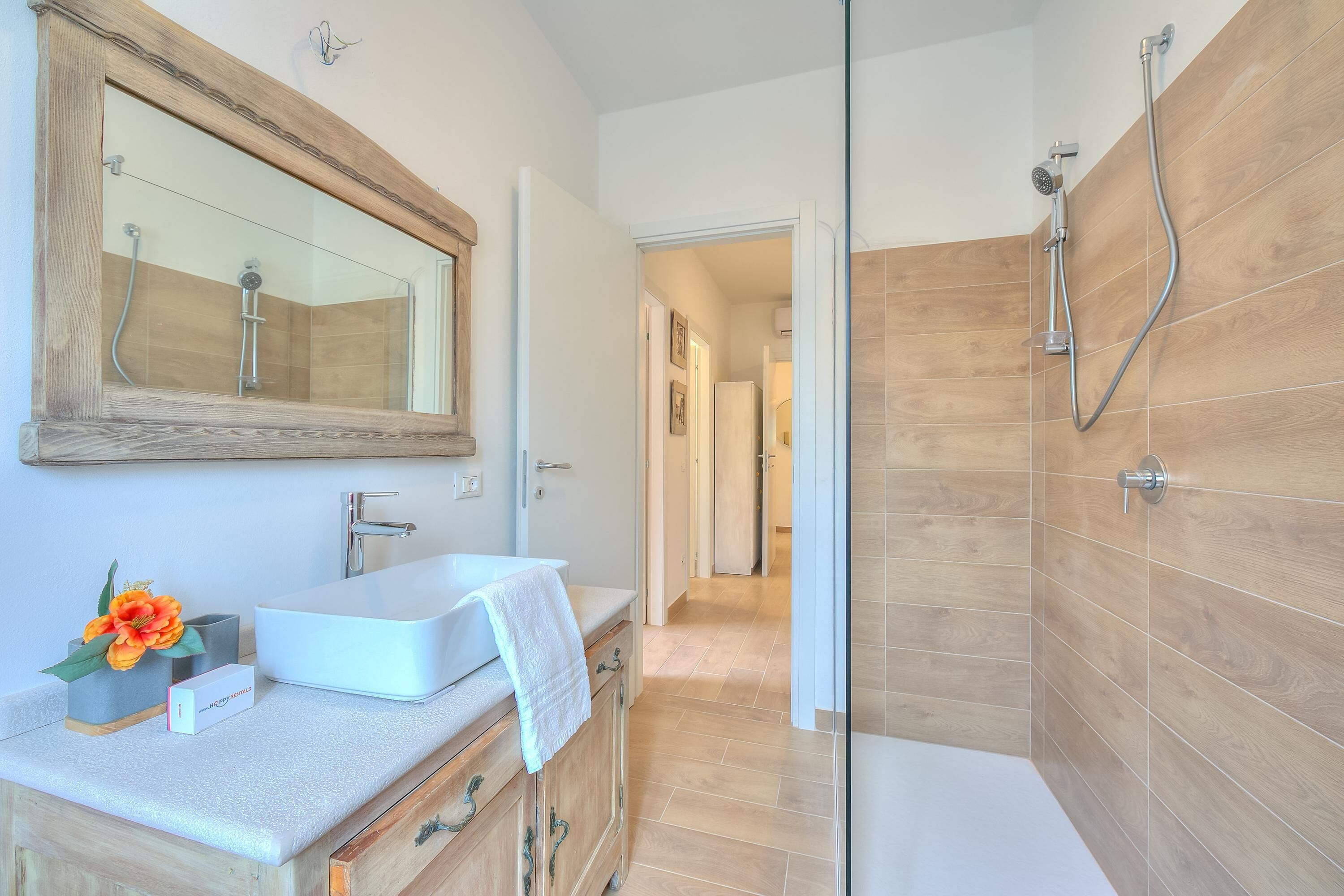 A modern bathroom with a glass shower enclosure, a white sink, and wooden cabinetry.