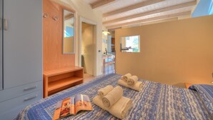 A bedroom with a bed, a wooden wardrobe, a mirror, and a window.