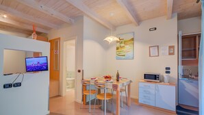 A modern kitchen with a dining area, wooden ceiling, and a flat-screen TV on the wall.