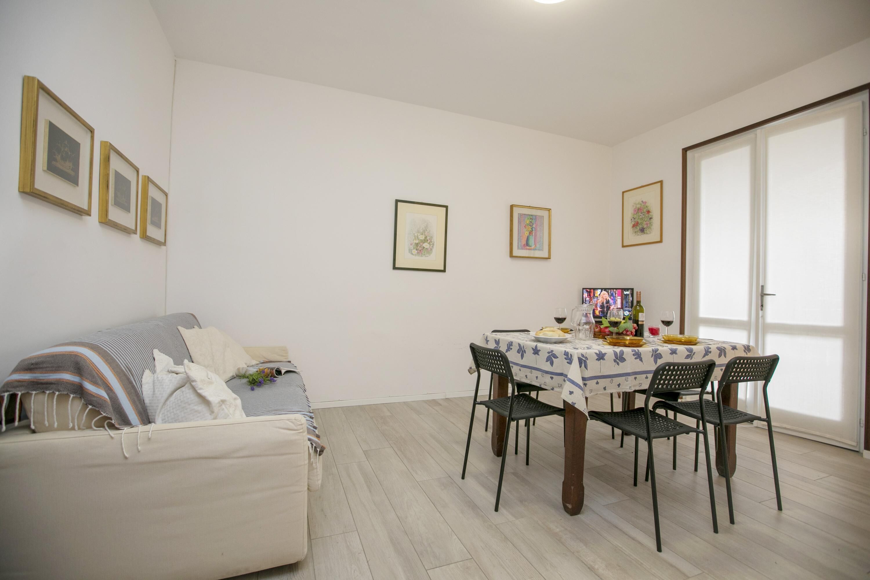 A dining area with a table set for four, a sofa, and framed pictures on the wall.