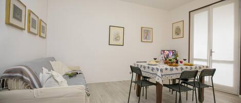 A dining area with a table set for four, a sofa, and framed pictures on the wall.