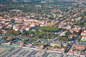 An aerial view of a densely populated urban area with a mix of residential and commercial buildings, a central green space, and a large parking lot.