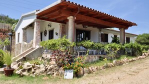 A two-story house with a wooden pergola, stone pillars, and a garden with various plants and flowers.