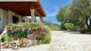 A stone-paved courtyard with a covered patio, lush greenery, and a stone wall.