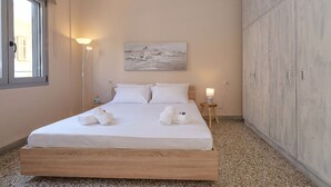 Un dormitorio con cama de madera, ropa de cama blanca, un cuadro en la pared y un armario.