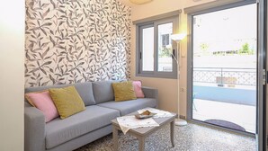 Una sala de estar con sofá gris, papel tapiz estampado, una mesita con bandeja y un ventanal corredero que da a un espacio exterior.