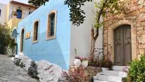 Una estrecha calle adoquinada bordeada por edificios de fachada azul y un muro de piedra.