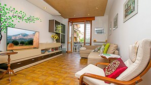 A living room with a large flat-screen TV, a sofa, a wooden chair, and a dining area with a table and chairs. - Appartamento Verona For You (Verona)