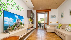 A living room with a large flat-screen TV, a sofa, a dining table, and a kitchen area with cabinets and a countertop. - Appartamento Verona For You (Verona)