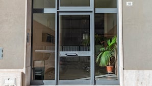 A modern building entrance with a glass door, a potted plant, and a visible number '18' on the wall. - House of the Gozzo in Monopoli (Monopoli)
