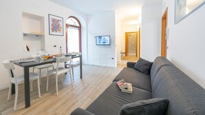 Un salon moderne avec un canapé gris, une table à manger et des chaises, et un téléviseur fixé au mur.