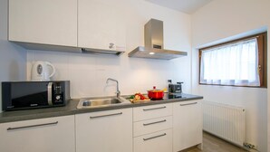 Une cuisine moderne avec des meubles blancs, un évier en acier inoxydable, un four à micro-ondes, une casserole rouge et une fenêtre avec des rideaux.
