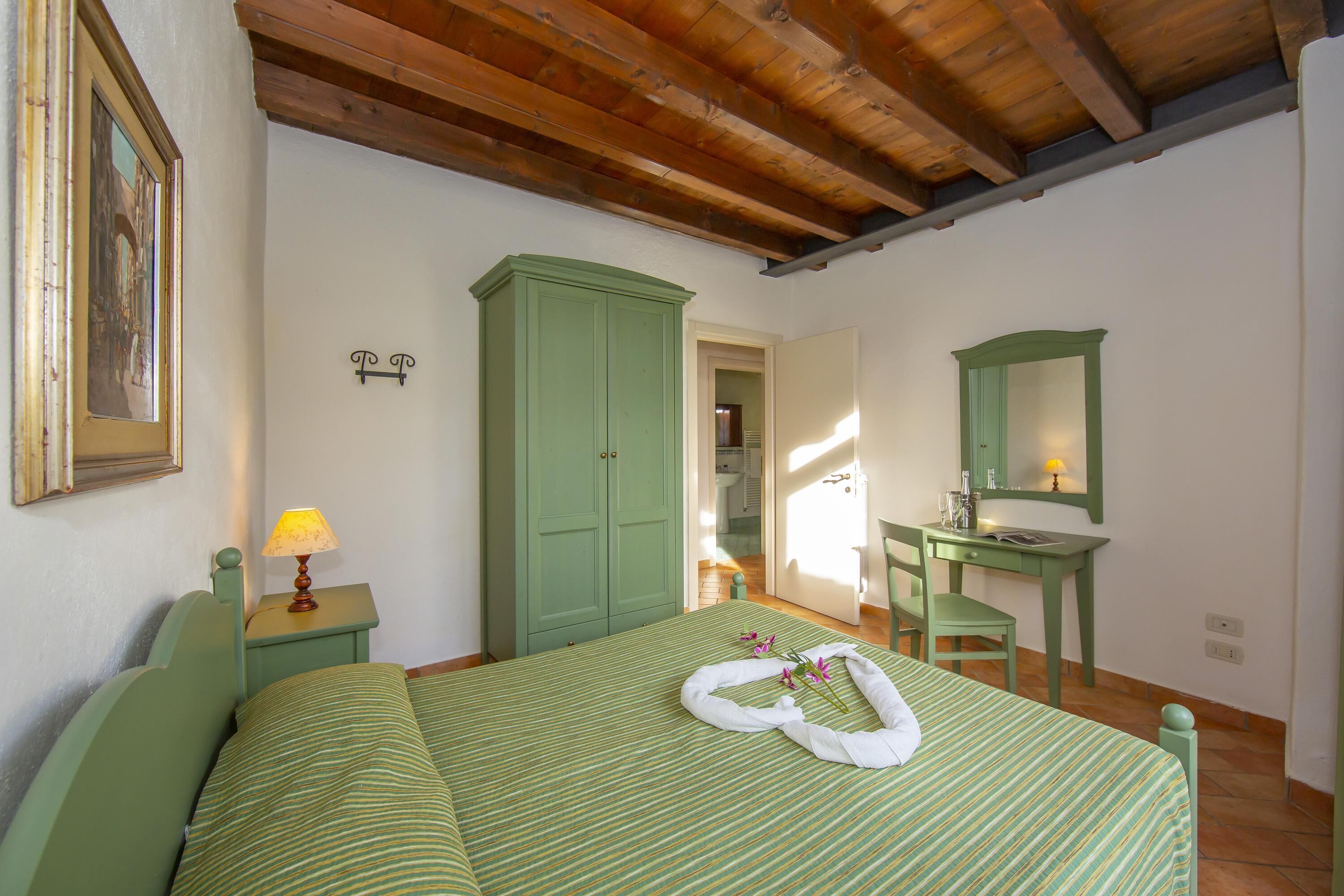 A room with a bed, a desk, a chair, a wardrobe, and a painting on the wall.