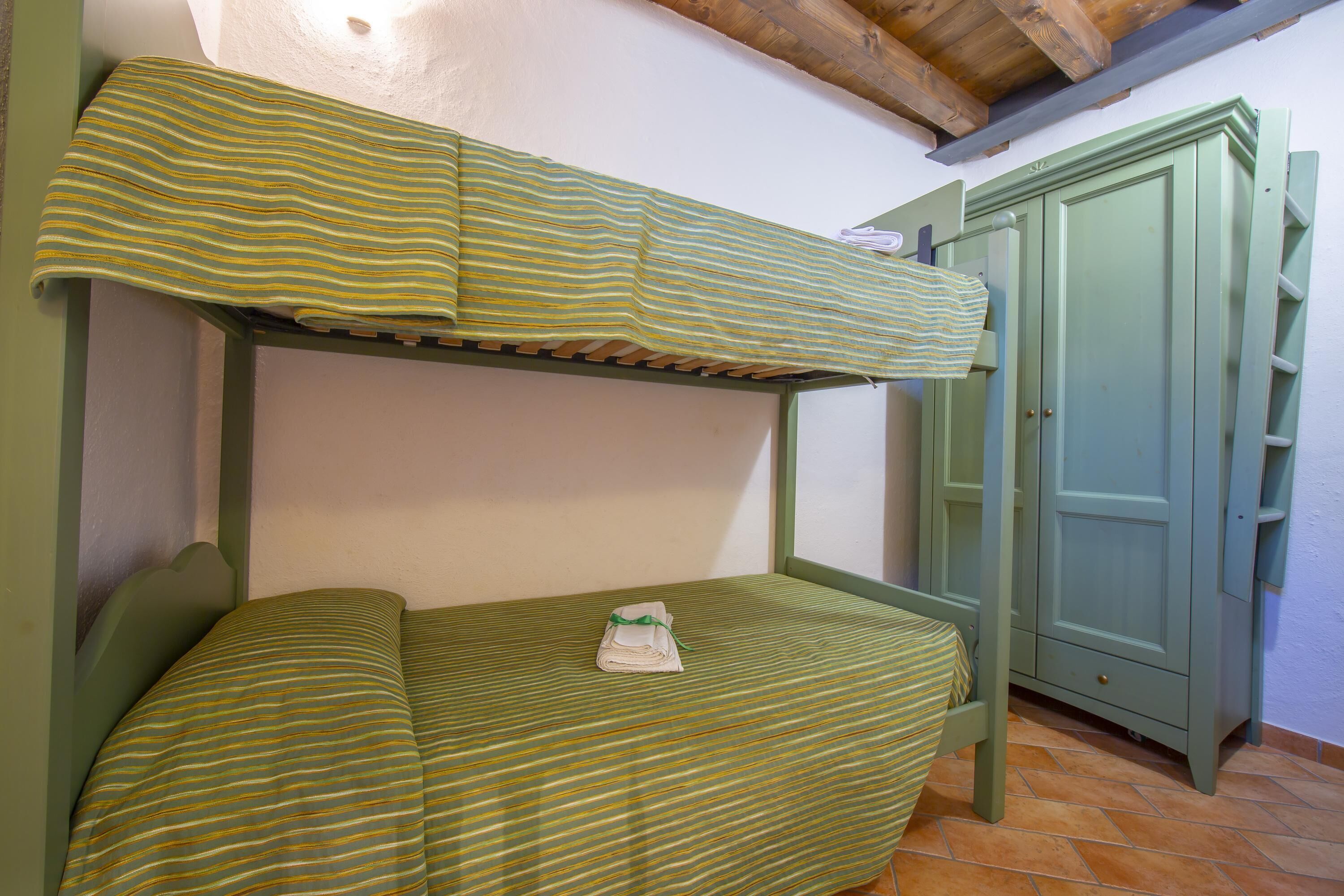 Ein Etagenbett mit gestreifter Bettwäsche, ein grüner Kleiderschrank und ein Fliesenboden.