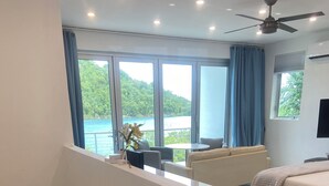 A modern bedroom with a large bed, a sofa, and a view of the outdoors through large windows.