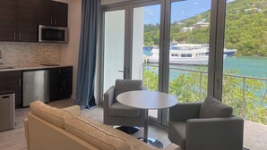 A modern kitchen with dark cabinets and a stainless steel microwave, a dining area with a round table and two chairs, and large windows offering a view of boats and greenery.