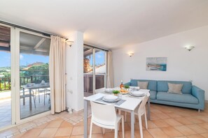 A dining area with a table set for four, a blue sofa, and a painting on the wall. - Feel So Good in Bunthe (Olbia)
