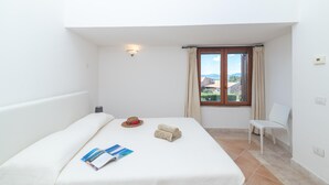 A hotel room with a bed, a window with curtains, a chair, and a wall-mounted light. - Feel So Good in Bunthe (Olbia)