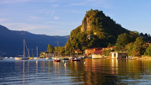 Une ville côtière où des bateaux sont amarrés le long de la rive, une colline imposante surmontée d’une église et un ciel dégagé.