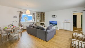 Un salon moderne avec un canapé gris, une table à manger en bois et des chaises. Un téléviseur est fixé au mur, et une cheminée est visible au fond.