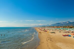 Ein Strand mit klarem, blauem Wasser, sandigem Ufer und einem Bergpanorama im Hintergrund.
