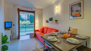 Un salon moderne comprenant un coin repas, un téléviseur et un balcon offrant une vue sur la verdure.