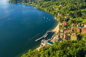 Vista aérea de un pueblo a orillas de un lago, con un puerto deportivo, edificios residenciales y abundante vegetación.
