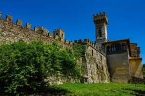 Un edificio storico in pietra con una torre, circondato da rigogliosa vegetazione.