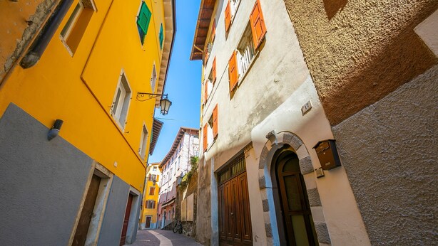 Eine schmale Kopfsteinpflasterstraße, gesäumt von farbenfrohen Gebäuden mit traditioneller Architektur, darunter ein markantes Rundbogenportal und ein Fahrrad davor.