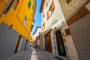 A narrow cobblestone street flanked by colorful buildings with traditional architecture, including a prominent arched doorway and a bicycle parked outside.