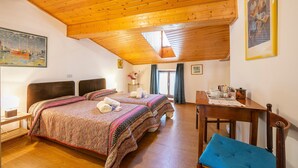 Ein Zimmer mit zwei Betten, Holzbalkendecke, einem Esstisch mit Stühlen und Kunstwerken an den Wänden.