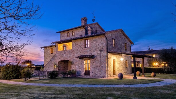 A stone house with multiple windows and a covered porch, surrounded by a well-maintained lawn. - Fratta Ginestre in Cortona (Cortona)