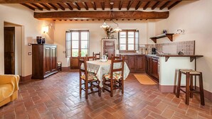 A spacious kitchen with wooden beams, a dining area with a table and chairs, and a yellow sofa. - Fratta Ginestre in Cortona (Cortona)