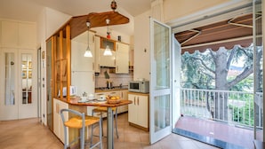 A kitchen with a dining area, a wooden ceiling fan, and a view of a tree through a glass door. - Gabri By The Sea in Diano Marina (Diano Marina)