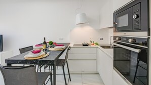 Una cocina moderna con comedor, que presenta una encimera negra, armarios blancos y horno con microondas integrados.