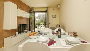 Un coin repas avec une table dressée pour deux personnes, un téléviseur et une vue sur l’extérieur.