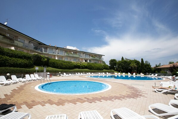 A pool area with multiple sun loungers and a building with balconies. - Casa Kristall Lago in Desenzano del Garda (Desenzano del Garda)