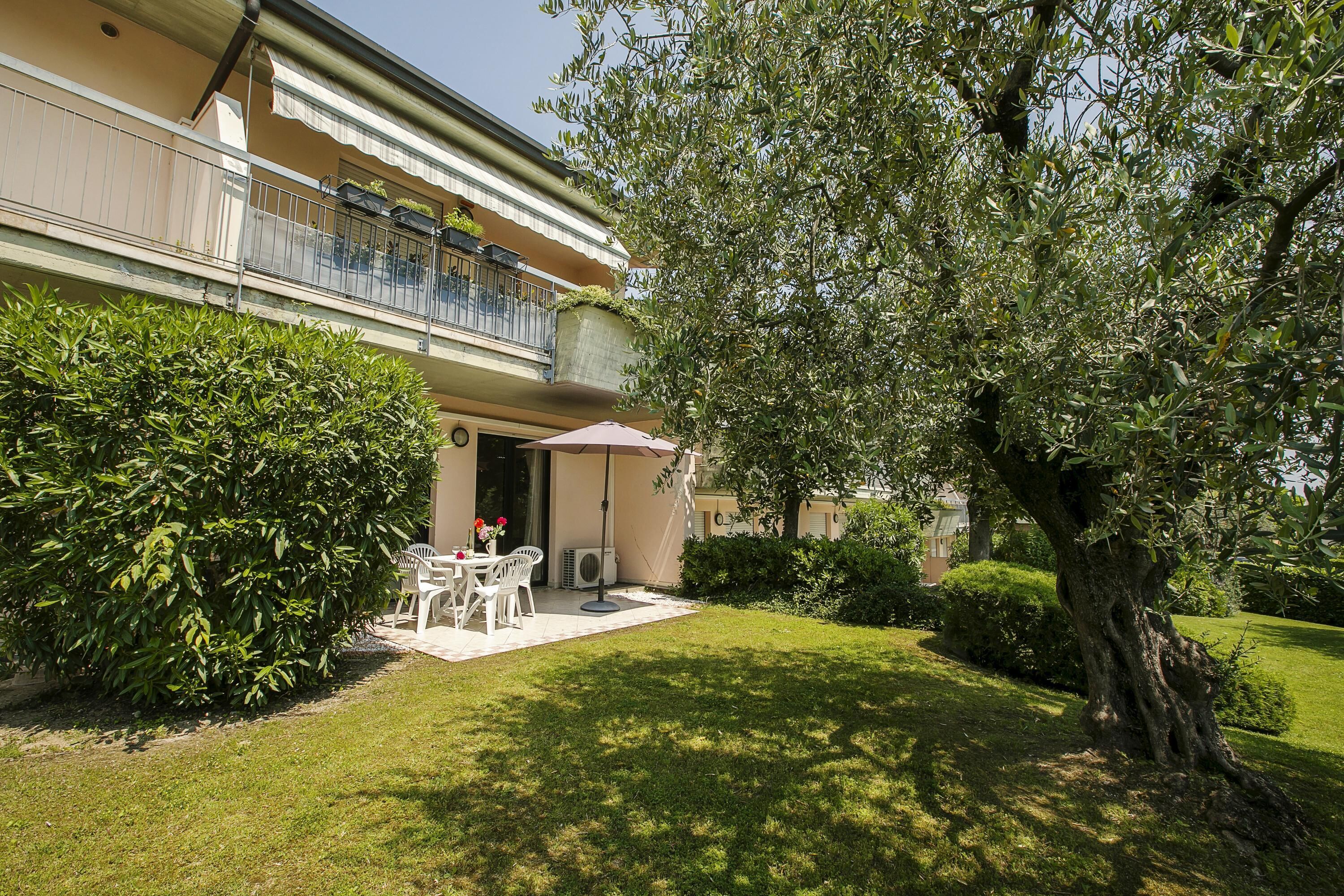 Un edificio con un balcone, un patio con mobili da esterno e un giardino curato.