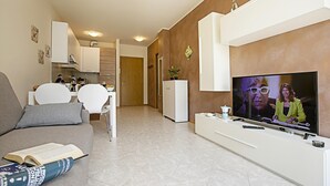 Un salon moderne avec un téléviseur à écran plat, un canapé, un coin repas et une cuisine en arrière-plan.