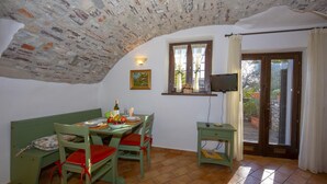 Un'area pranzo con soffitto in pietra, un tavolo apparecchiato per due e una televisione su un mobile.