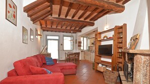 Un salon avec un canapé rouge, des poutres apparentes en bois au plafond, un téléviseur et une cheminée.