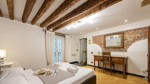 Une chambre avec un grand lit, des poutres en bois, un bureau et un miroir sur un mur en briques.