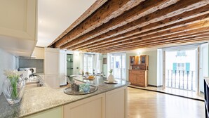 Une cuisine spacieuse dotée d’un grand îlot central, de poutres apparentes en bois au plafond et offrant une vue sur l’extérieur.