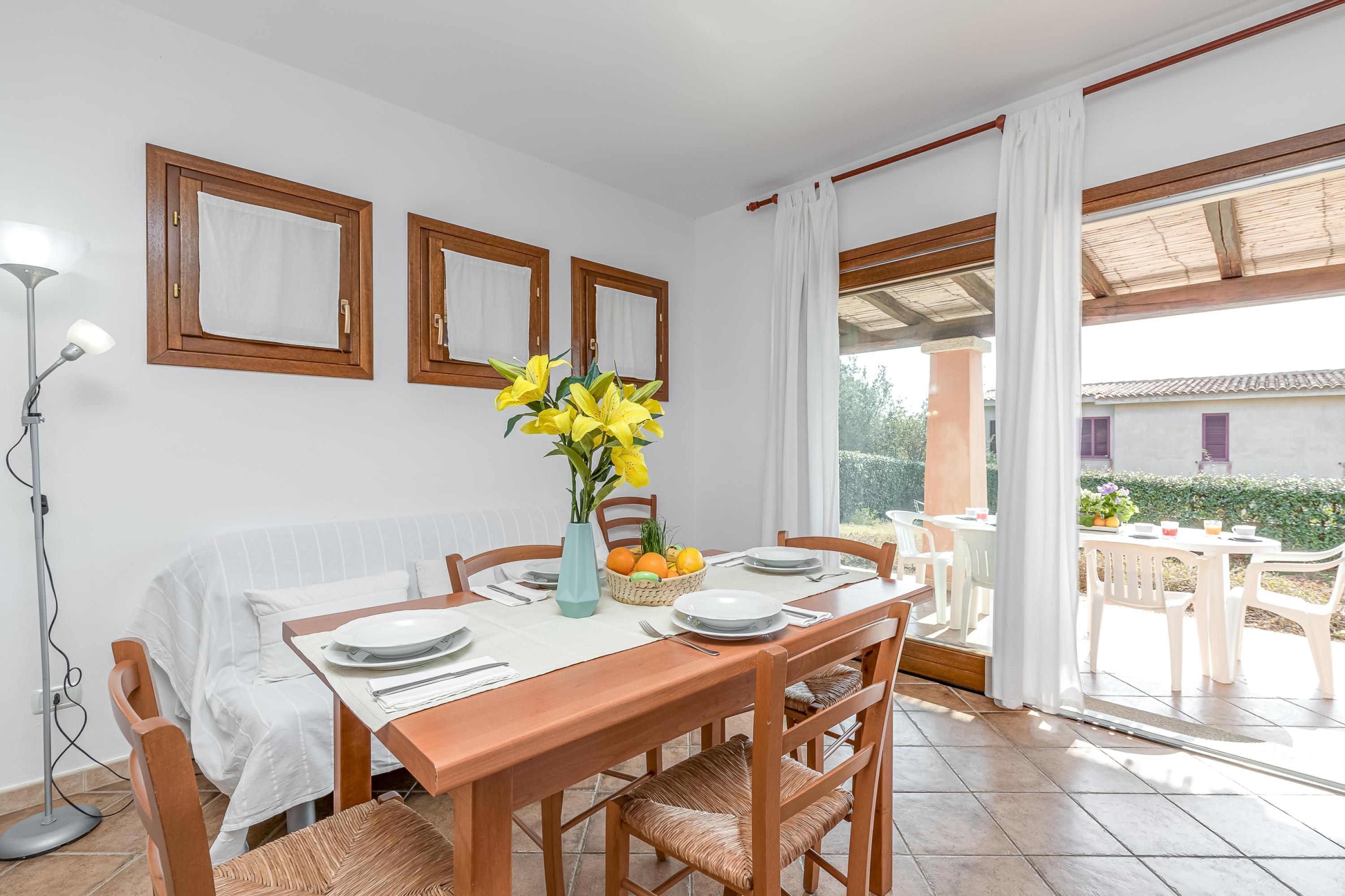 Un coin repas avec une table en bois, des chaises blanches et un vase rempli de fleurs jaunes.