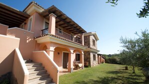 A two-story house with a balcony, a stone facade, and a well-maintained lawn. - Le Dimore di Nettuno 1 With Pool (Olbia)