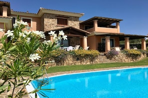 A two-story house with a swimming pool, stone walls, and outdoor seating.