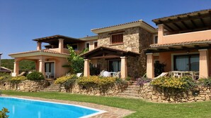 A poolside view of a resort with stone and stucco buildings, a swimming pool, and a well-maintained lawn. - Le Dimore di Nettuno 1 With Pool (Olbia)