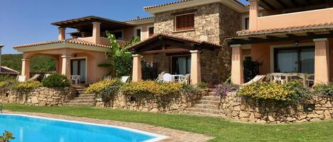 A poolside view of a resort with stone and stucco buildings, a swimming pool, and a well-maintained lawn.